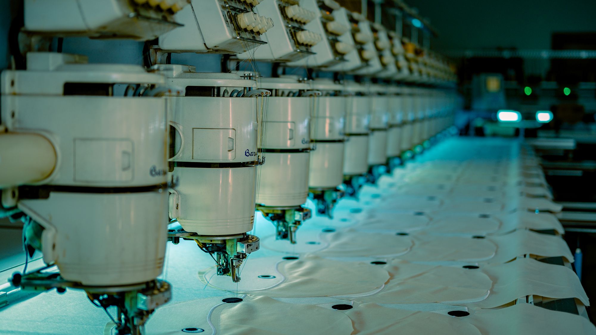 A row of industrial embroidery heads processing garment panels — reference photograph